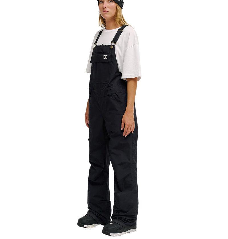 A person wearing a white t-shirt, black beanie, black boots, and DC Shoes Valiant Bib Pants stands facing slightly to the side against a white background.