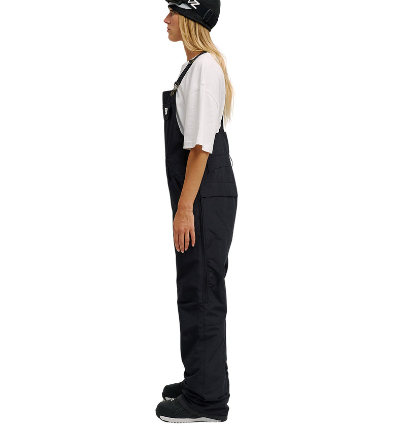 Woman in profile view wearing a white t-shirt, black beanie, black shoes, and the Valiant Bib Pants by DC Shoes, standing against a plain white background—an outfit that balances style with breathable protection for all-day comfort.