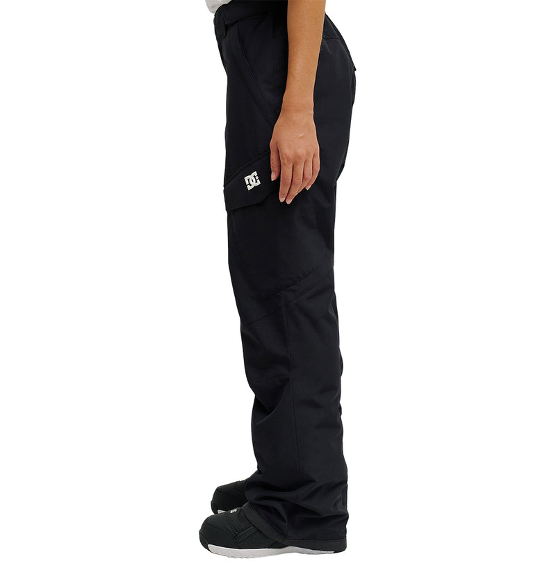 A person is standing in profile view against a white background, wearing the DC Shoes Nonchalant Pant—black, waterproof insulated cargo pants with a DC logo on the pocket—and black and white shoes.