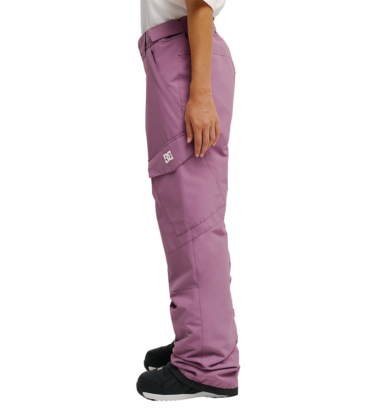 A person stands in profile against a plain white background wearing mauve Nonchalant Pants by DC Shoes, featuring a white DC logo on the side pocket, paired with black shoes and a white shirt.