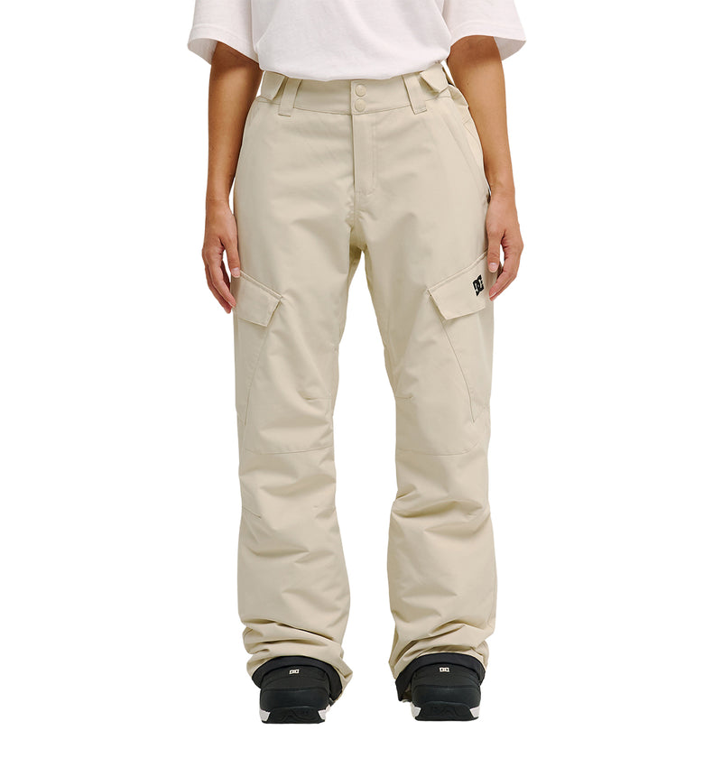 A person wearing the DC Shoes Nonchalant Pants—loose, beige insulated cargo pants with large side pockets, belt loops, and enhanced waterproofing for improved snow performance—along with a white t-shirt and black shoes stands facing forward.