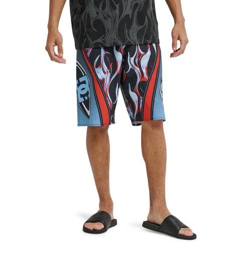 A person wearing Reebok Sylem 21 black slide sandals and bold flame-patterned knee-length shorts, with only their legs and lower torso visible, stands against a white background.
