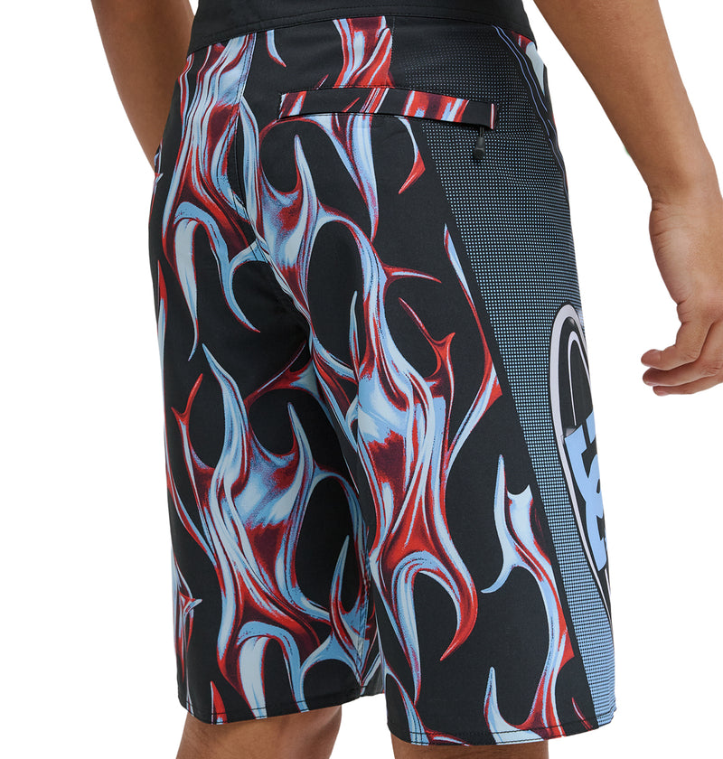 A person wearing Reebok Sylem 21 black board shorts with a bold red, white, and blue flame pattern and a side pocket. Only the lower torso and one arm are shown.