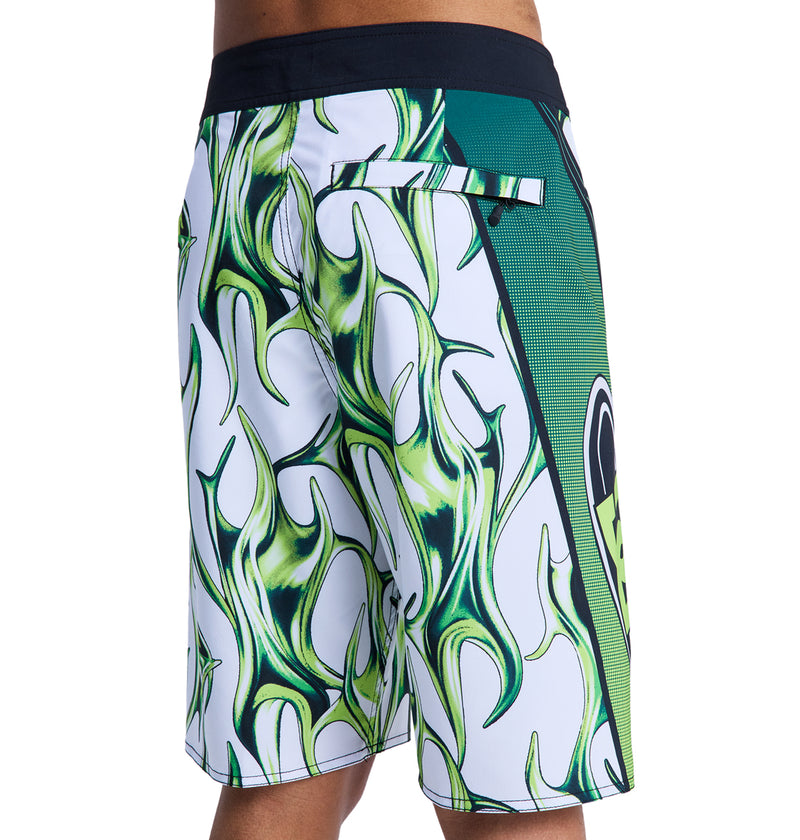 A person shown from the side and waist down wearing Reebok Sylem 21 white and green board shorts with an abstract flame design and a back pocket.