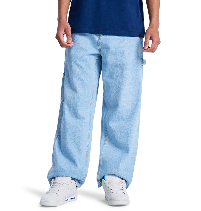 A person wears DC Shoes Men's Baggy Denim Carpenter Pant in light blue, paired with a dark blue T-shirt and white sneakers. Only the lower half of the body is visible against a plain white background.