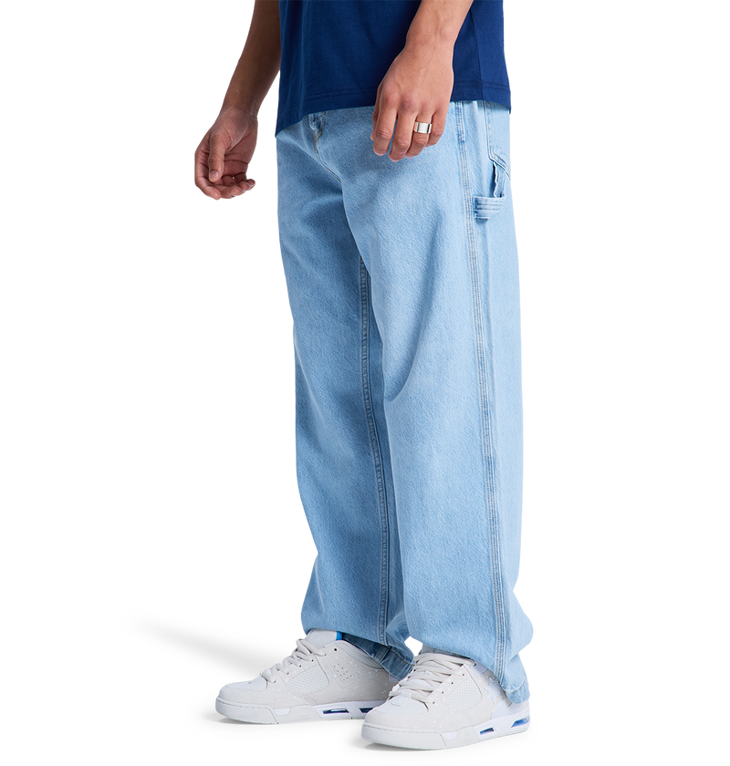 Only the lower half is visible as someone models the DC Shoes Men's Baggy Denim Carpenter Pant, a wide-leg fit jean, paired with a dark blue shirt and white sneakers against a white background.
