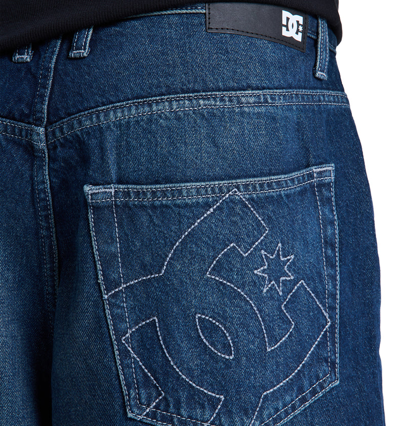 Close-up of the back pocket of blue Baggy Denim Jort by Reebok, featuring a large stitched Reebok logo on the pocket and a black Reebok label above the pocket near the waistband.