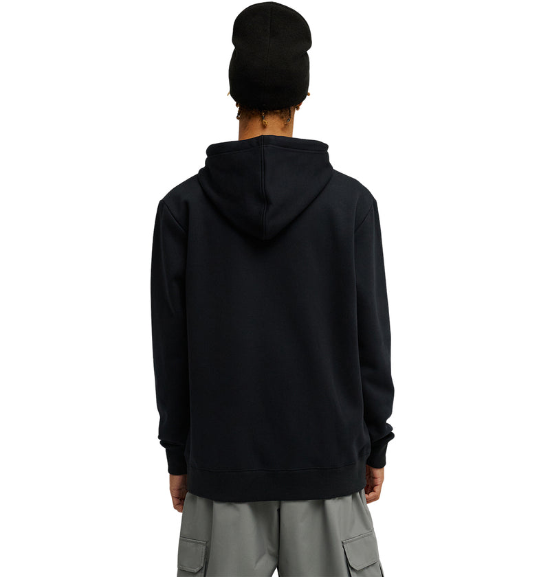 A person wearing the DC Shoes Snowstar black hoodie with a comfortable fit, paired with gray cargo pants and a black beanie, stands facing away from the camera against a plain white background.