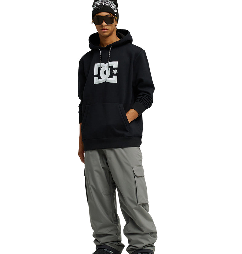 A person wearing the Snowstar black hoodie from DC Shoes with a comfortable fit, gray cargo pants, sunglasses, a black beanie, and a chain necklace stands with one hand in their pocket against a white background.