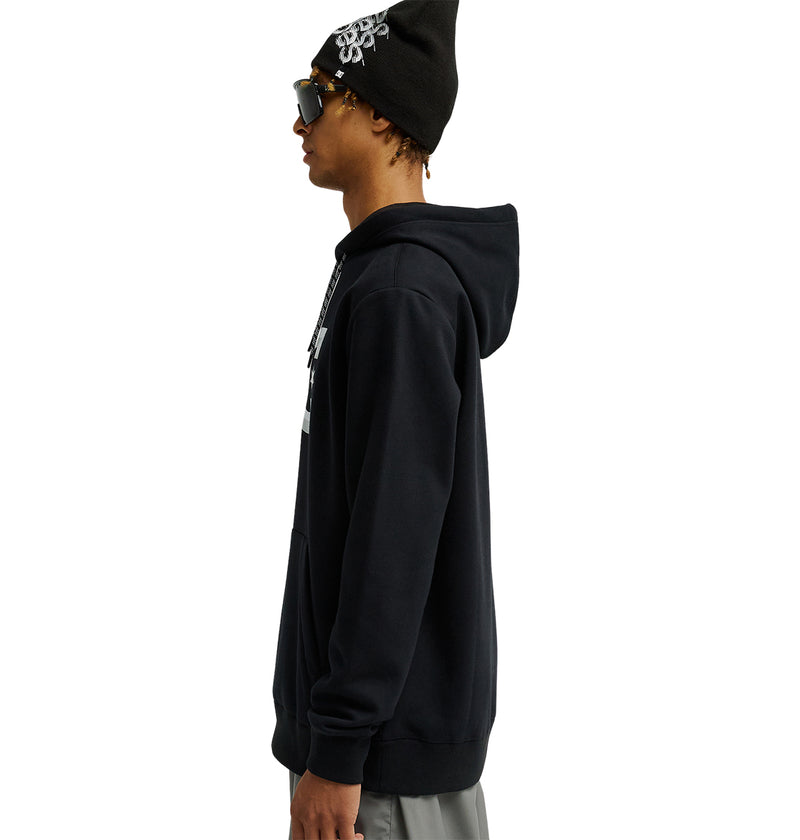 A person models the DC Shoes Snowstar black hoodie and matching beanie, featuring a white design and sunglasses, standing in profile against a white background to showcase the weather protection and comfortable fit.