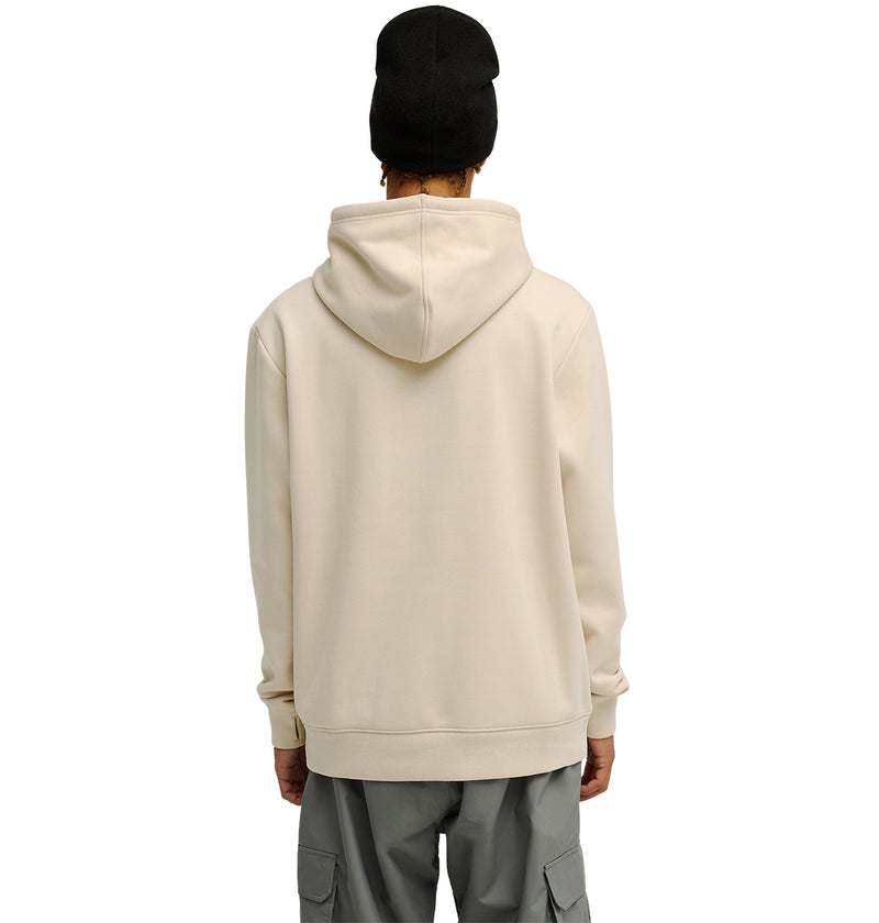 A person wearing the DC Shoes Snowstar light beige hoodie, paired with gray cargo pants and a black beanie, stands facing away against a plain white background.