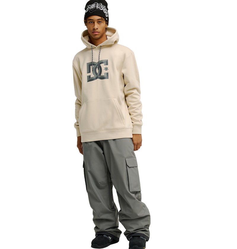 A person wearing the beige DC Shoes “Snowstar” hoodie with a comfortable fit, along with gray cargo pants, black shoes, and a black beanie stands facing forward against a white background.