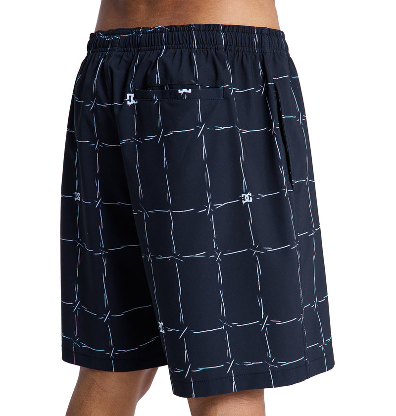 A person wearing Reebok DC Wired Volley 19 shorts—black with a white grid and barbed wire pattern, featuring an elastic waistband and a small buttoned back pocket.
