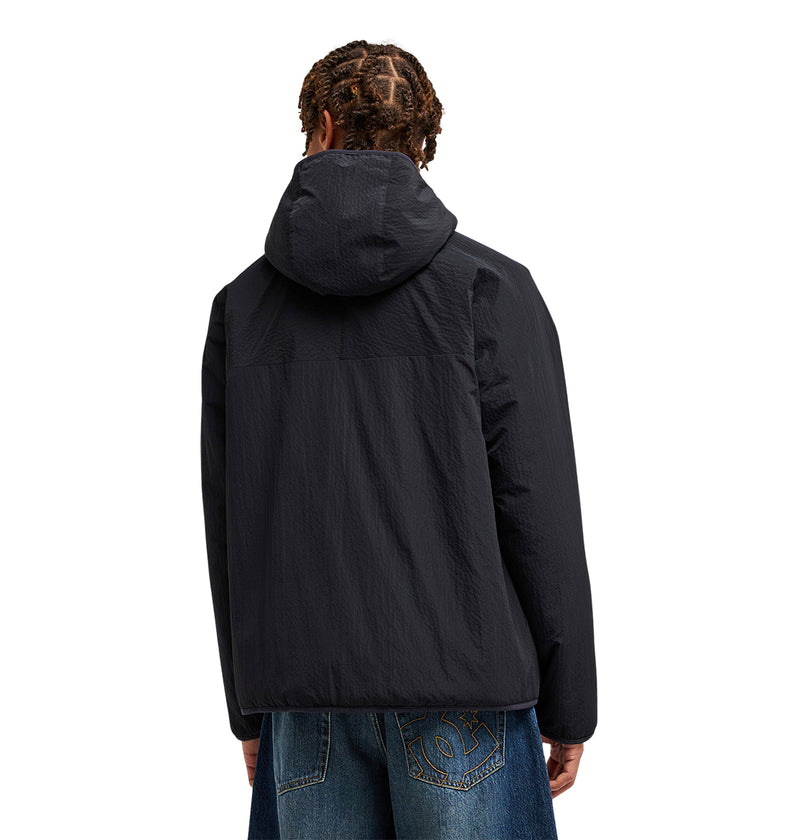 A person is seen from behind, standing against a plain white background, wearing blue jeans and the DC Shoes Coldstag Sherpa Reversible black hooded jacket.