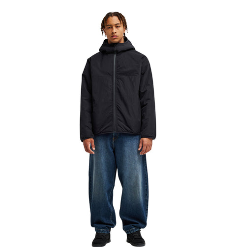 A person wearing the DC Shoes Coldstag Sherpa Reversible hooded jacket in black, paired with loose blue jeans and black shoes, stands facing forward against a plain white background.