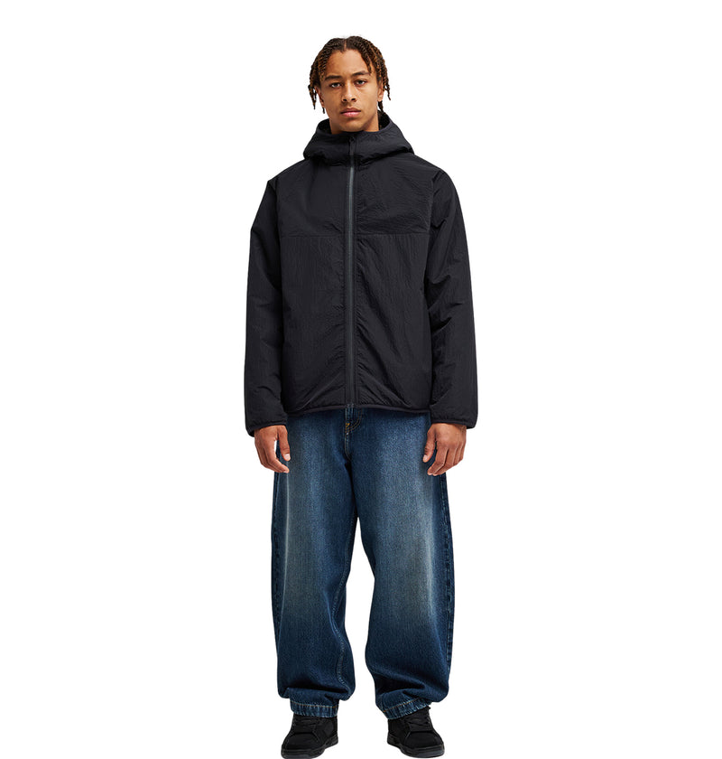 A person wearing the DC Shoes Coldstag Sherpa Reversible hooded jacket in black, paired with loose blue jeans and black shoes, stands facing forward against a plain white background.