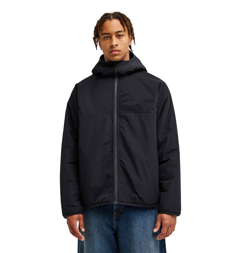 A person wearing the DC Shoes Coldstag Sherpa Reversible jacket, known for its cold-weather comfort, and blue jeans stands facing forward against a plain white background.