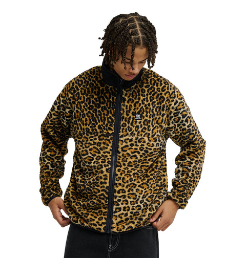 A person wearing the DC Shoes Lynx Fleece—a black and brown leopard print zip-up jacket featuring a small chest logo—holds the hem with both hands and looks down, exemplifying cold-weather comfort in this soft fleece style.