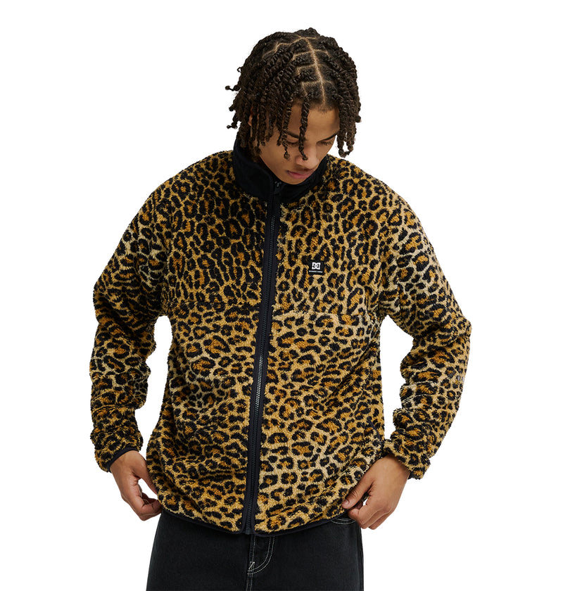 A person wearing the DC Shoes Lynx Fleece—a black and brown leopard print zip-up jacket featuring a small chest logo—holds the hem with both hands and looks down, exemplifying cold-weather comfort in this soft fleece style.