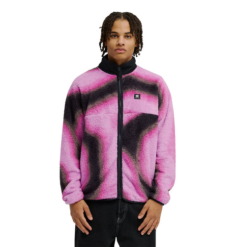 A person wearing the DC Shoes Lynx Fleece, a soft pink and black jacket with a black collar, stands against a white background, looking directly at the camera with their hands relaxed by their sides.