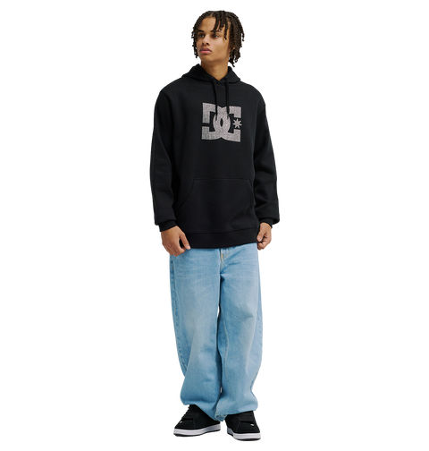 A person wearing the Men’s DC Strass Star Hoodie by DC Shoes, styled in black, pairs it with light blue baggy jeans and black sneakers while standing facing slightly to the right against a plain white background.