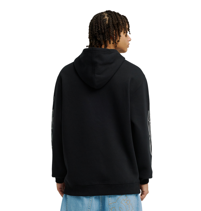 A person with short twists wears the DC Shoes Men's Side Flame Hoodie, a black pullover known for its fleece warmth, along with light blue jeans, facing away from the camera against a plain white background.