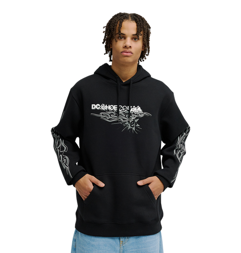A person wearing the Men's Side Flame Hoodie from DC Shoes—a black pullover featuring bold white DC graphics on the front and sleeves—stands with hands in the spacious front pocket against a simple, light backdrop. The hoodie’s fleece construction delivers cozy warmth and stylish comfort to the overall look.