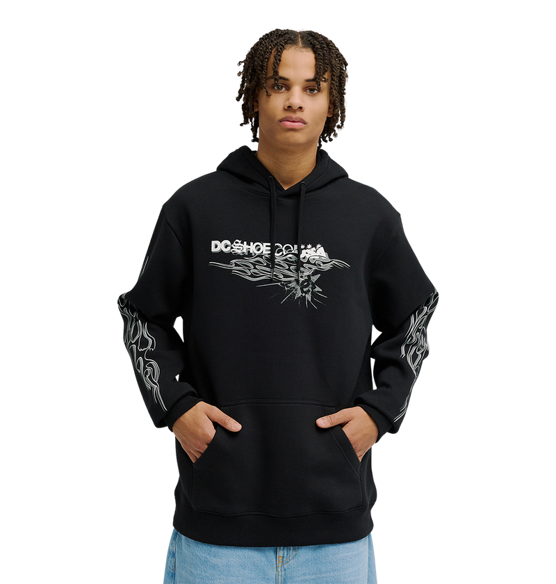 A person wearing the Men's Side Flame Hoodie from DC Shoes—a black pullover featuring bold white DC graphics on the front and sleeves—stands with hands in the spacious front pocket against a simple, light backdrop. The hoodie’s fleece construction delivers cozy warmth and stylish comfort to the overall look.