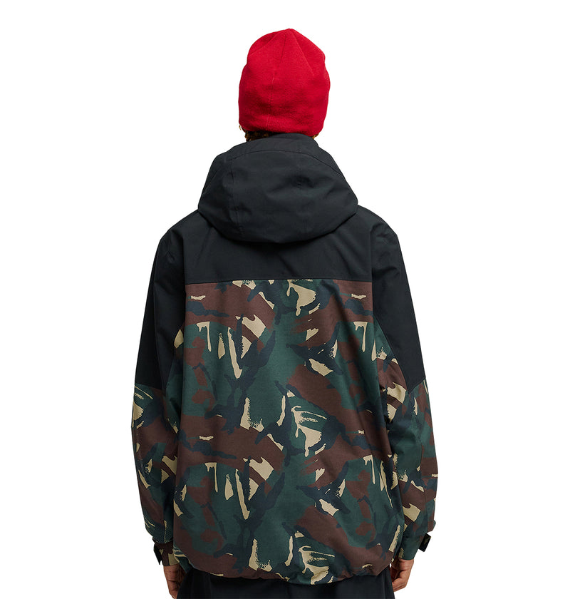 A person wearing a red beanie and the DC Shoes Edge Jacket 20K—a black and camouflage snow jacket engineered for top-tier performance—stands with their back to the camera against a white background.