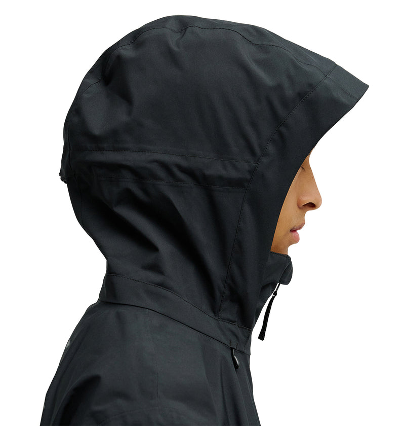 A person in profile view wears the DC Shoes Edge Jacket 20K—a black hooded jacket with the hood up, crafted for exceptional waterproofing and snow performance—against a white background.
