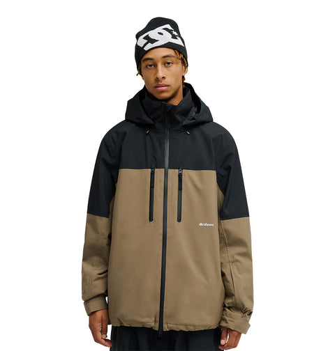 A person stands facing forward with their hands at their sides against a plain white background, wearing the DC Shoes Edge Jacket 20K—a black and brown waterproof jacket with a hood—and a black beanie featuring a white logo.