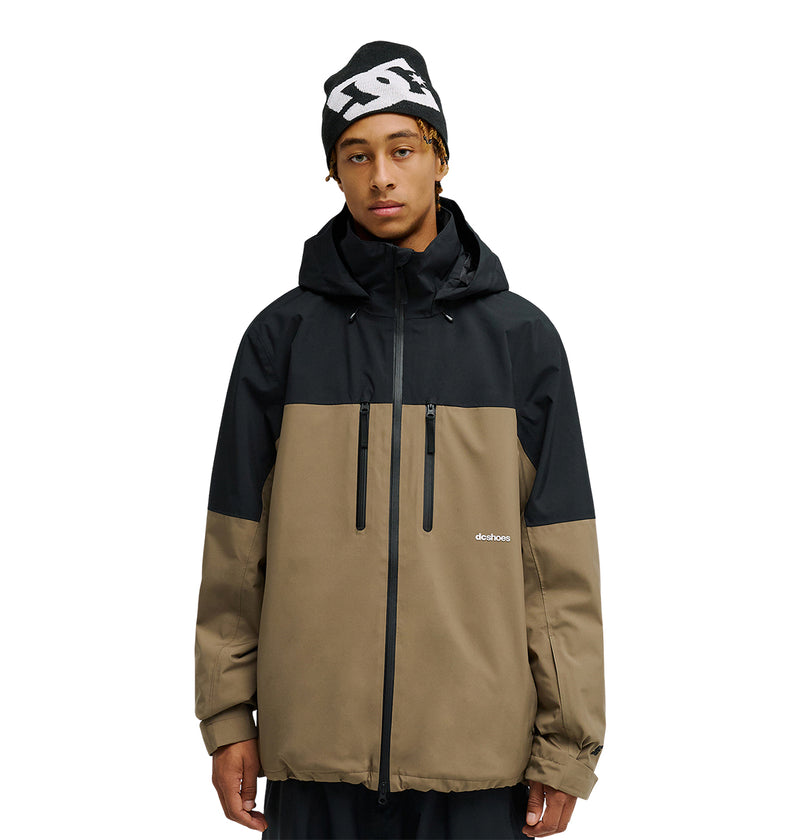 A person stands facing forward with their hands at their sides against a plain white background, wearing the DC Shoes Edge Jacket 20K—a black and brown waterproof jacket with a hood—and a black beanie featuring a white logo.