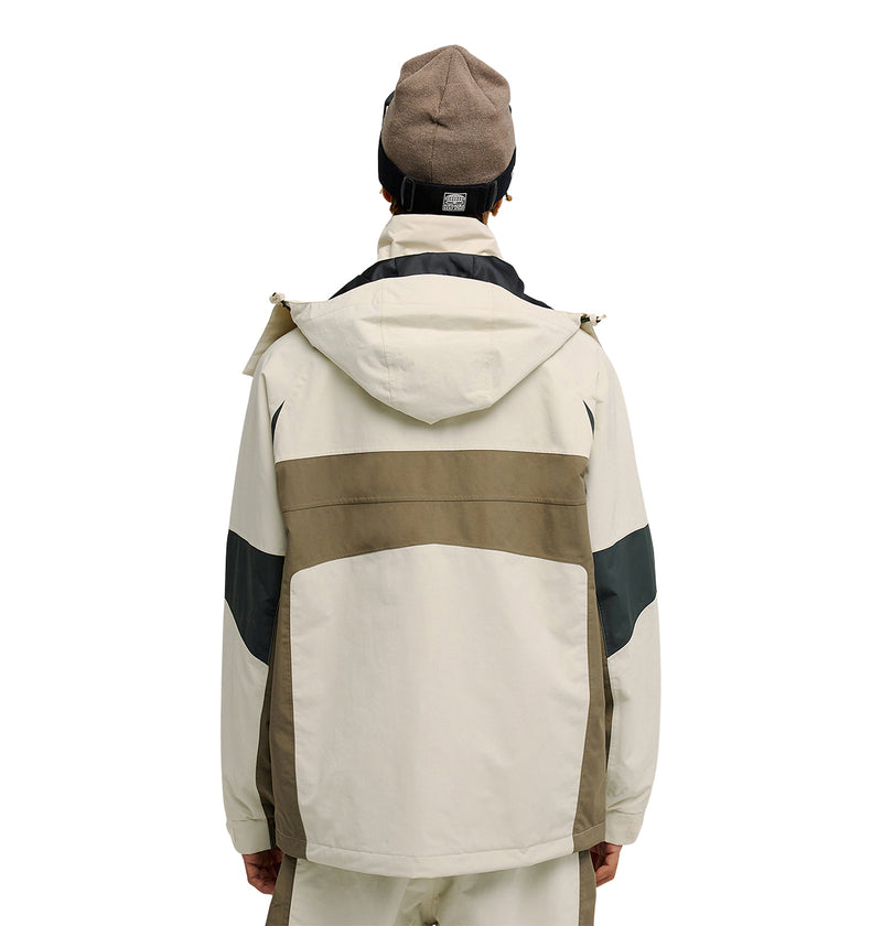A person is seen from the back wearing the DC Shoes Mountain Lab Jacket 20K—a hooded, color-blocked jacket in beige, brown, and black designed for breathable protection. They also sport a brown beanie and light-colored pants while standing against a plain white background.