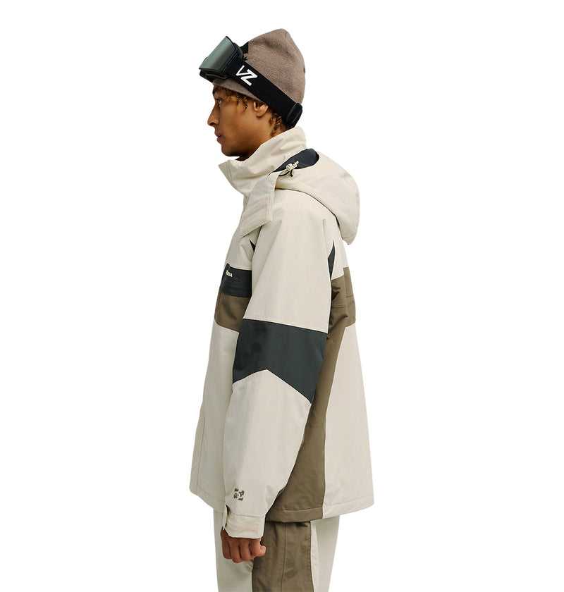 A person is shown in profile facing left against a plain white background, wearing the DC Shoes Mountain Lab Jacket 20K in a beige and olive colorway, paired with beige pants and a brown beanie topped with ski goggles—the jacket features advanced waterproofing and breathable protection.