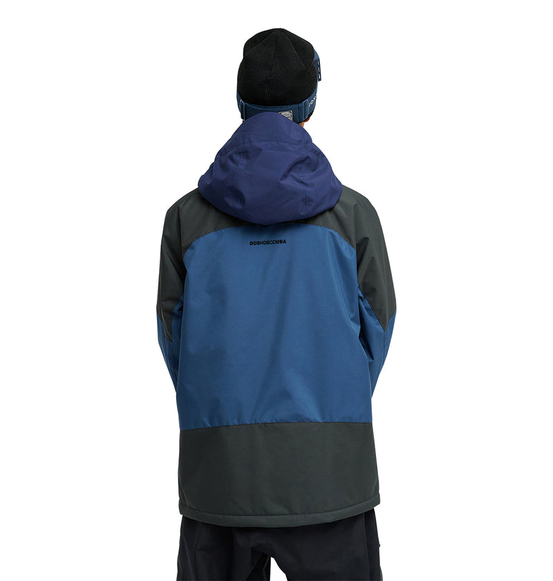A person wearing the DC Shoes Coldsmoke Jacket 10K—a blue and gray hooded jacket designed for breathable protection and snow performance—along with a black beanie, stands with their back to the camera against a plain background.