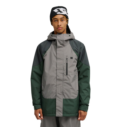 A person stands facing forward with a neutral expression against a plain white background, wearing the DC Shoes Coldsmoke Jacket 10K—a gray and green hooded jacket designed with waterproof and breathable protection.