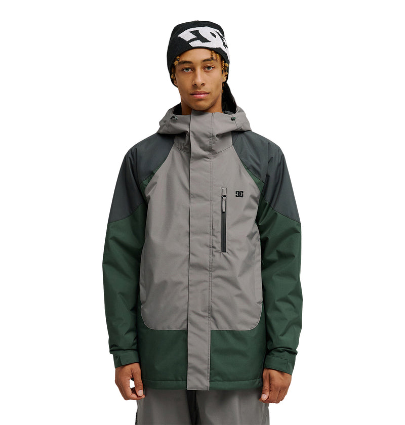 A person stands facing forward with a neutral expression against a plain white background, wearing the DC Shoes Coldsmoke Jacket 10K—a gray and green hooded jacket designed with waterproof and breathable protection.