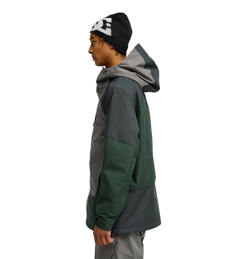 A person wearing the DC Shoes Coldsmoke Jacket 10K in green and gray, featuring waterproof and breathable protection, along with gray pants and a black beanie with white patterns, stands in profile facing left against a white background.