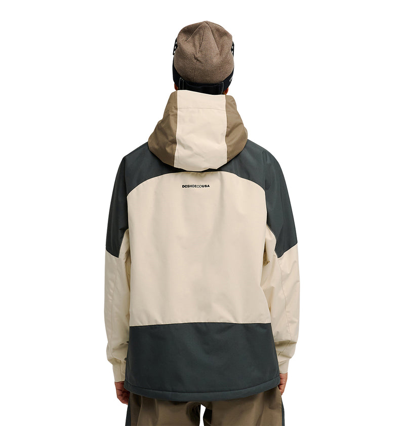 A person wearing the DC Shoes Coldsmoke Jacket 10K in beige and dark green, featuring breathable protection and a small logo near the shoulders on the back, paired with a brown beanie and facing away from the camera.