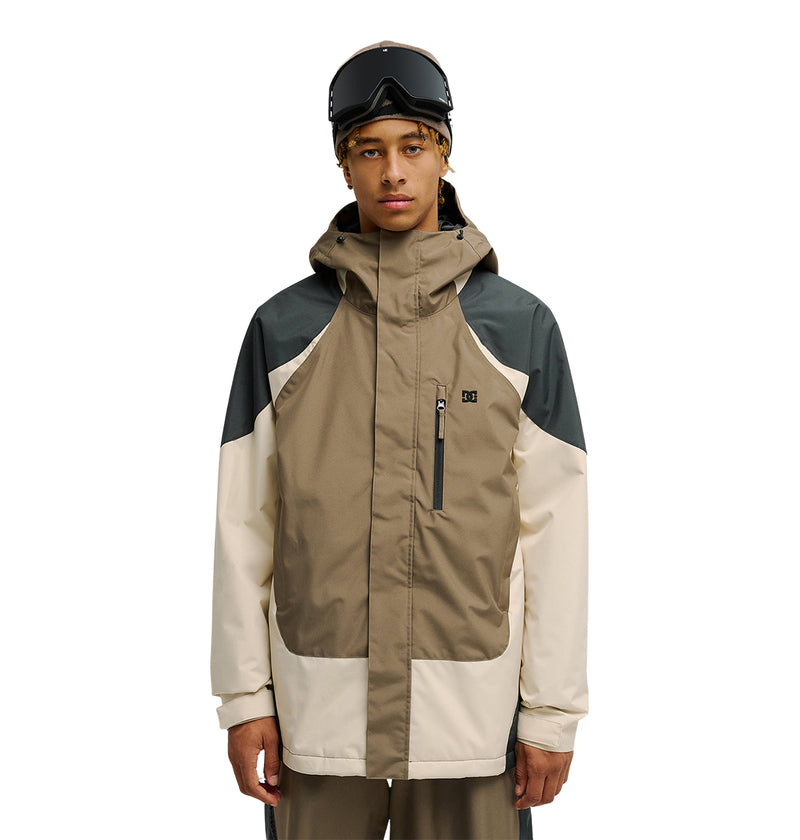 A person wearing ski goggles and the DC Shoes Coldsmoke Jacket 10K—a color-blocked beige, tan, and dark gray winter jacket with a hood, designed for breathable protection—stands against a white background.