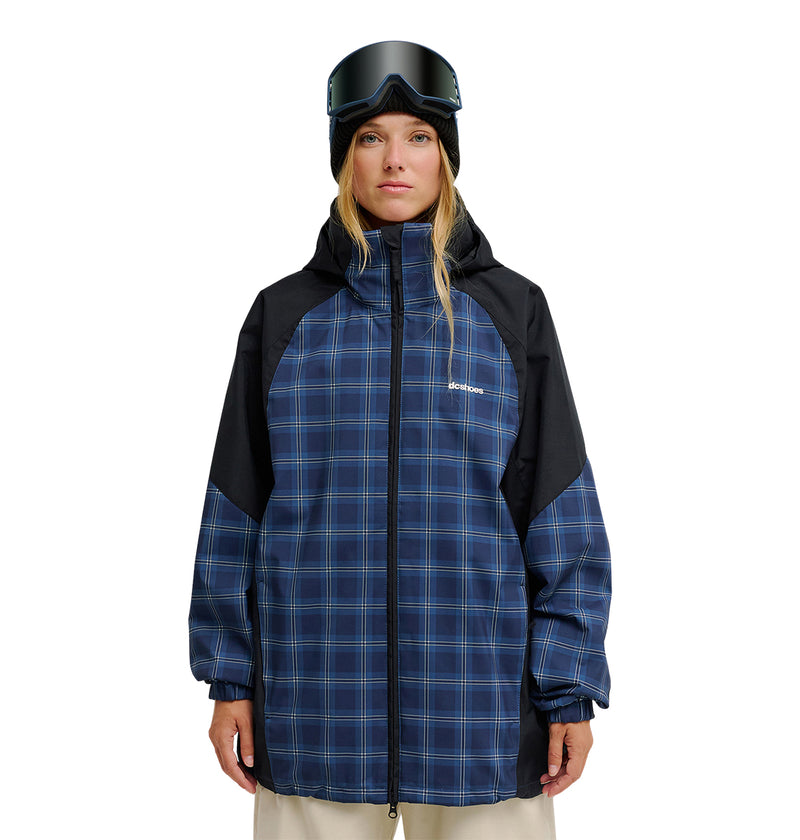 A woman wearing the DC Shoes Trackstar Jacket 10K—a blue plaid jacket designed for breathable protection—along with beige pants, a black beanie, and ski goggles stands facing forward against a white background.