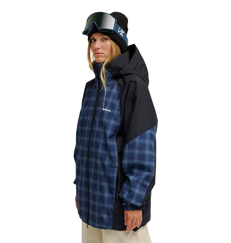 A person wearing the DC Shoes Trackstar Jacket 10K—a blue plaid winter jacket that offers breathable protection and superior waterproofing—along with a black beanie and ski goggles, stands facing slightly sideways against a white background.