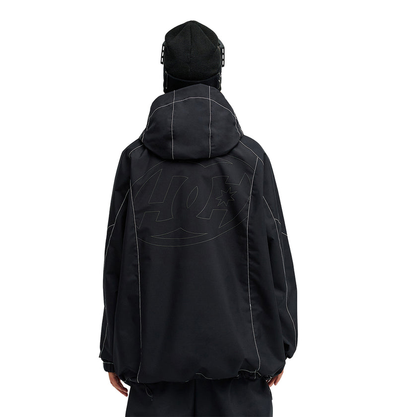 A person stands with their back to the camera, dressed in a loose black DC Shoes Trackstar Jacket 10K featuring prominent white stitching and a subtle oversized logo. Designed for snow performance, this jacket provides breathable protection ideal for cold weather. The individual also sports a black beanie.