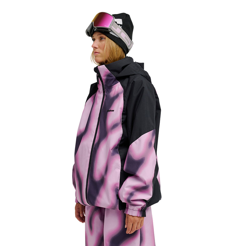 A person wearing the DC Shoes Trackstar Jacket 10K—a black and pink patterned ski jacket with breathable protection—along with matching pants, a black beanie, and ski goggles stands facing left against a white background.