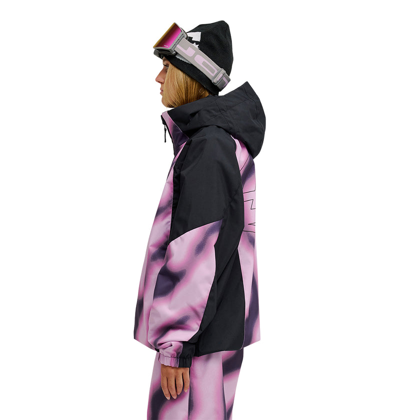 Person in ski gear, wearing the DC Shoes Trackstar Jacket 10K—engineered for breathable protection and snow performance—in black and pink, matching pants, a black beanie, and ski goggles; standing in profile view facing left against a white background.