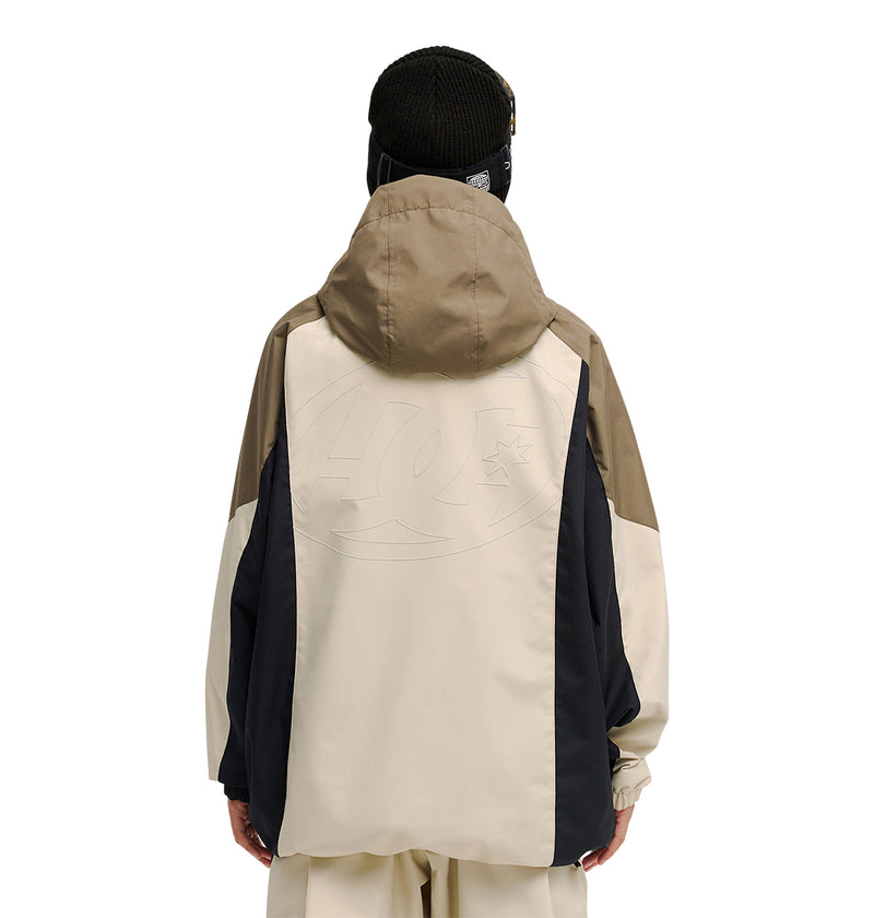 A person is seen from behind wearing the DC Shoes Trackstar Jacket 10K in beige, black, and brown, paired with matching pants. Designed for snow performance, the jacket offers breathable protection and features a subtle logo on the back. The look is completed with a black knit beanie.