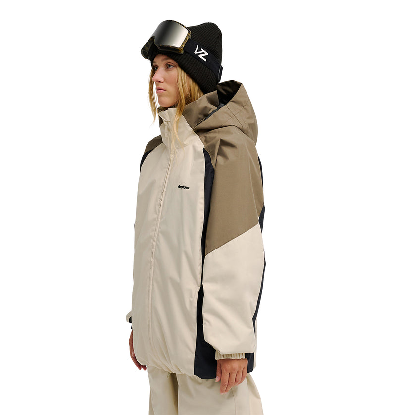 A person wearing the DC Shoes Trackstar Jacket 10K, a tan hooded winter jacket with breathable protection, along with beige pants, a black beanie, and ski goggles stands facing sideways against a white background.