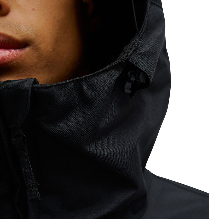 Close-up of a person wearing the DC Shoes Basis Jacket 10K in black, featuring a hood with visible drawstring details and part of their face, set against a white background.