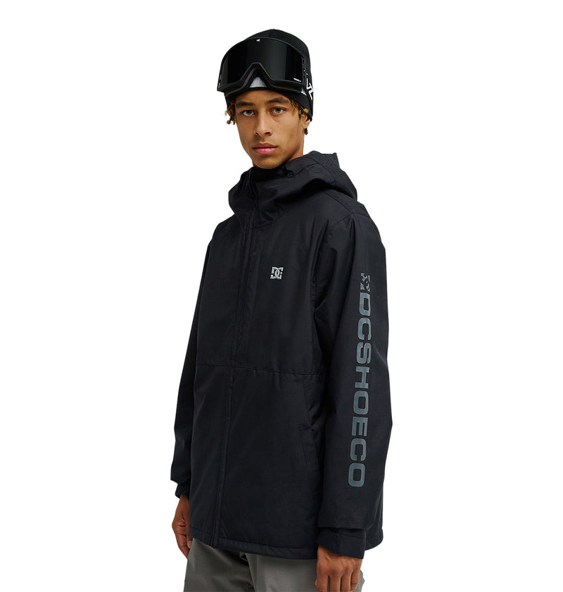 Wearing the DC Shoes Basis Jacket 10K in black, featuring DCSHOECO branding on the sleeve, and dark ski goggles on their head, a person stands against a plain white background.