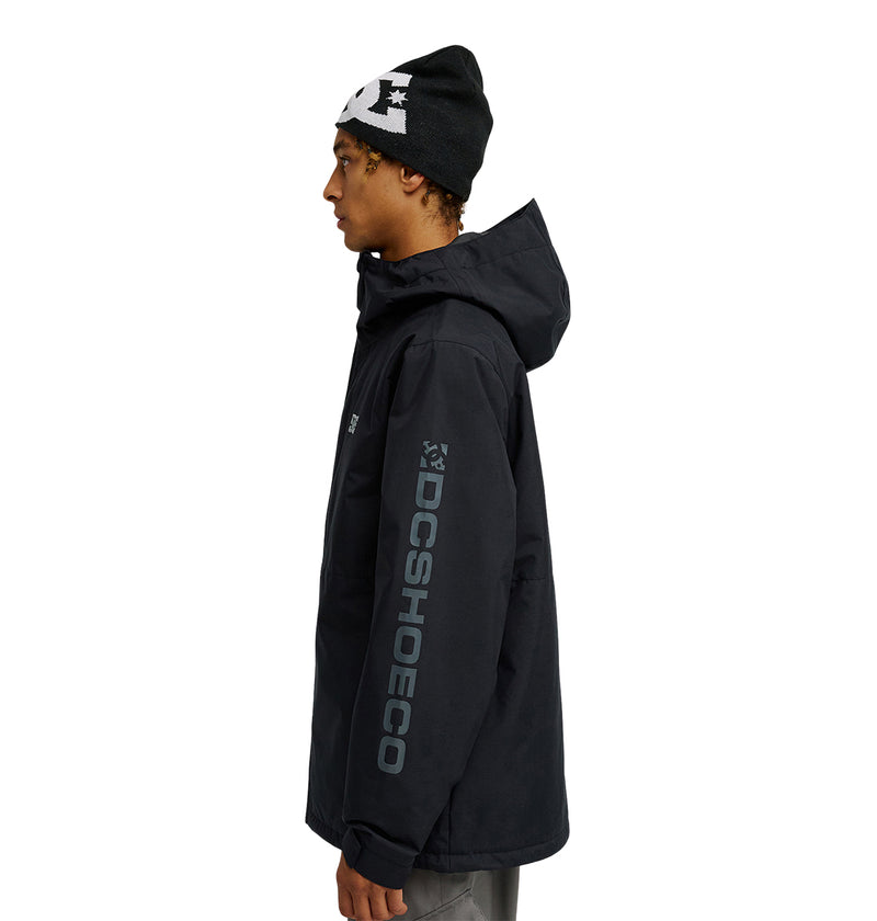 A person in the DC Shoes Basis Jacket 10K, a black insulated jacket featuring DCSHOECO on the sleeve, and a black beanie stands in profile against a white background.